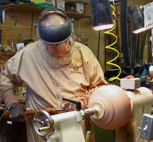 Artist shaping the exterior of a large piece of wood using a heavy duty gouge.