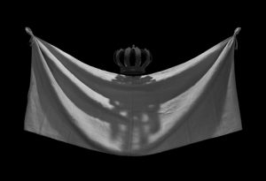 A black and white photograph of a royal crown with a tapestry in front of it