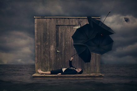 A photograph of a man laying down, balancing multiple umbrellas on his arm