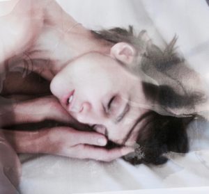 A photograph of a woman sleeping on white sheets