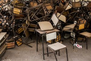 A photograph of a large number of school chairs haphazardly stacked on each other