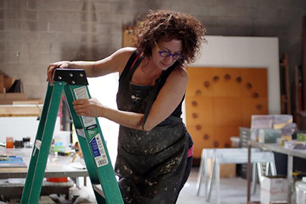 An artist looks down at her work from a ladder