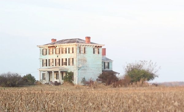 A photograph of an abandoned large house among a cornfield