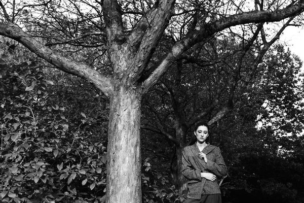 A black and white photograph of a woman standing beside a tall tree