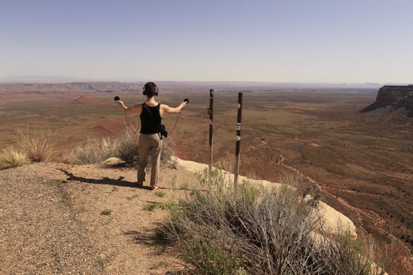 A sound artist stands at the peak of a mountain with recording devices