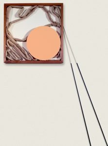 A collage of a circle and fabric in a wooden frame on a pale background
