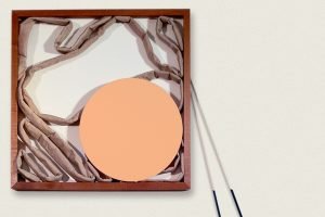 A collage of a circle and fabric in a wooden frame on a pale background