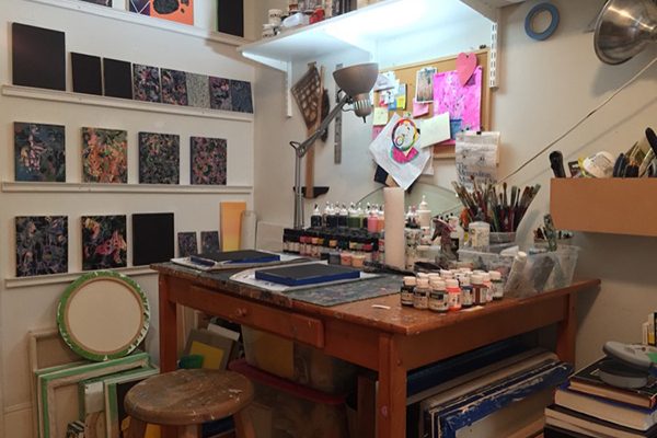 A collage artists studio, with paint bottles lining the desk and art on the walls