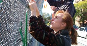 Artist Katherine Daniels threads fabric through a chain link fence for an art installation