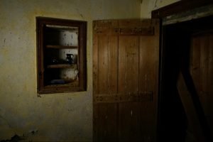 A still shot of an open door next to a pantry opening in an abandoned house