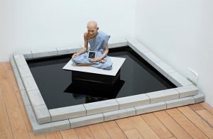 An installation of a buddha sitting in a black pool