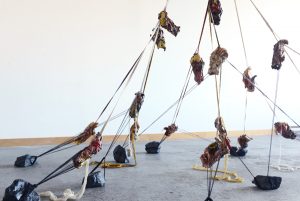 An installation of cords suspended from the ceiling, with cast hands climbing up the cords