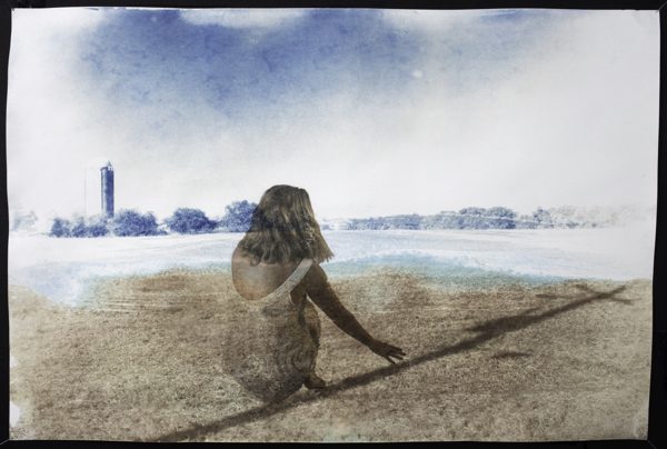 A photograph of a field with a silo in the background, with the shadowy figure of a girl in the foreground