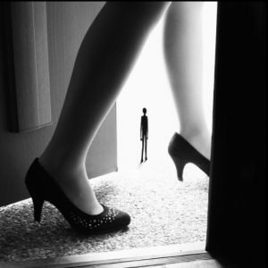 A close up photograph of a woman's feet walking through a doorway, with a small figure in between her calves