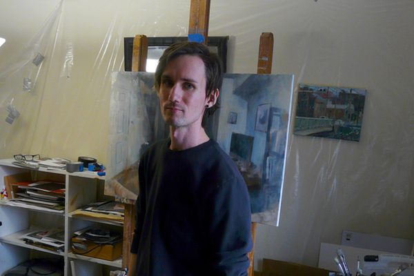 Painter Dillon Samuelson stands in his studio in front of his paintings