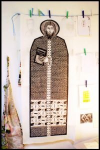 A large print of a drawing of the patron saint of printmakers, holding a text
