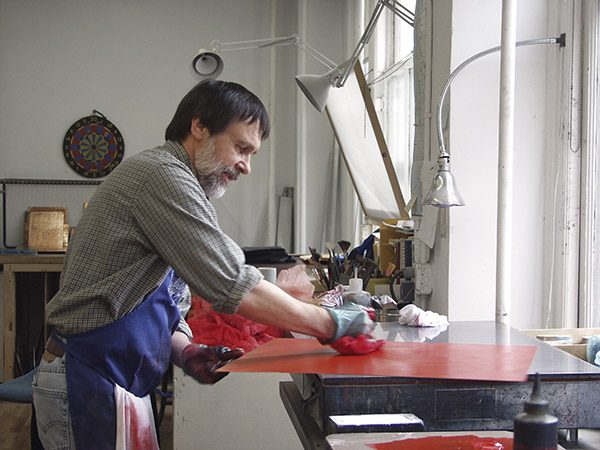 An artist inking a plate in his studio