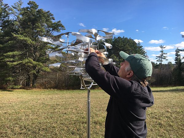 An artist repairs an element of his outdoor kinetic sculpture