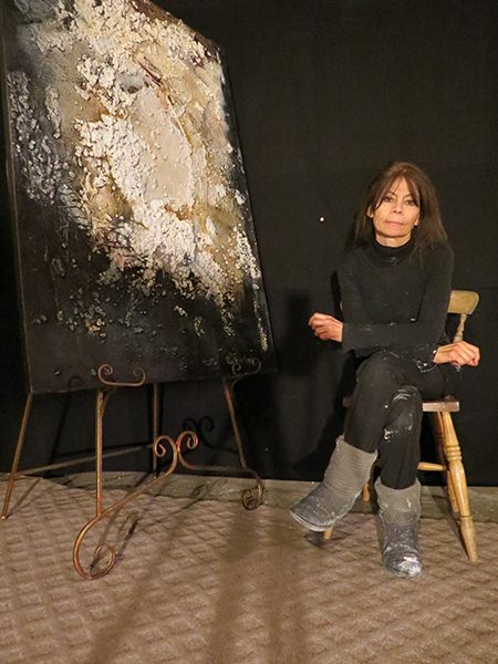 Painter Josie Bell sits next to one of her earthy abstract paintings