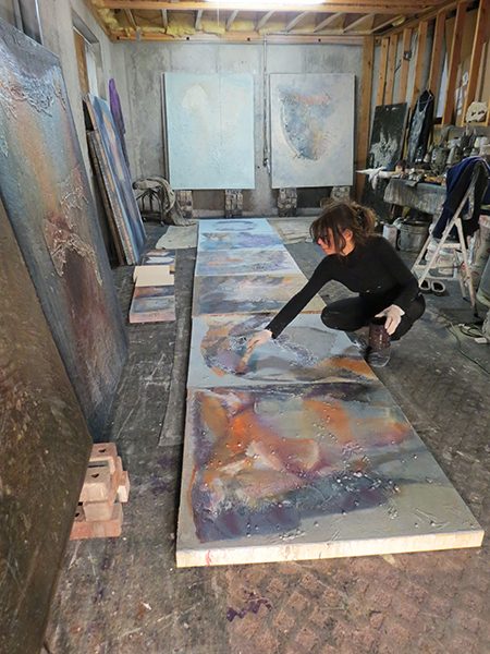 Josie Bell applies an oil glaze to her paintings on the floor of her studio