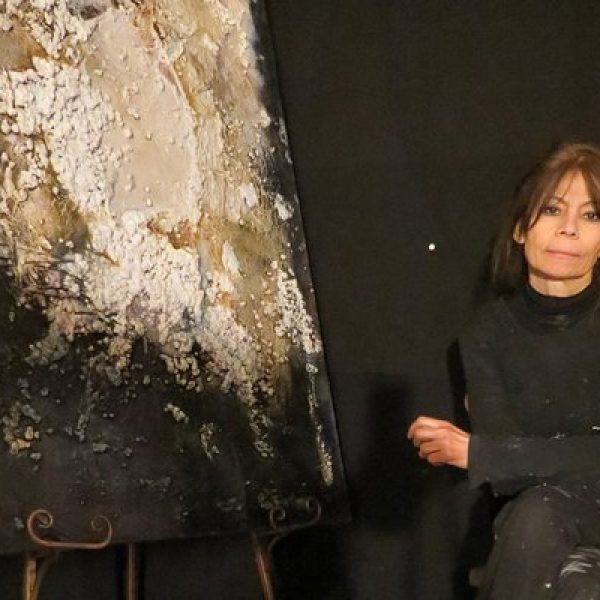 Painter Josie Bell sits next to one of her earthy abstract paintings
