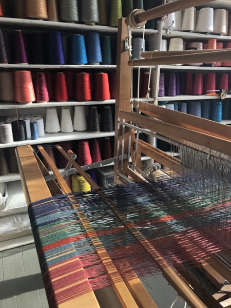 A close up of a loom with jewel-toned thread