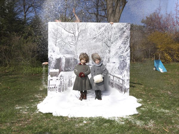 A photograph of two children posing in front of a wintry backdrop, on a non-snowy day