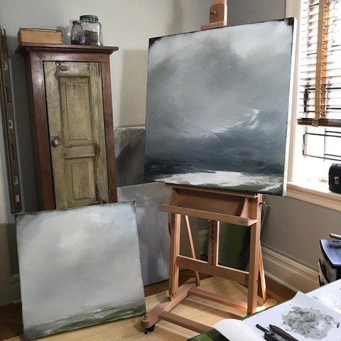 An abstract oil painting of the ocean hangs on an easel in the artist's studio