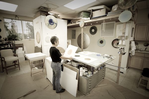 A sepia-toned photograph of an artist working in her studio