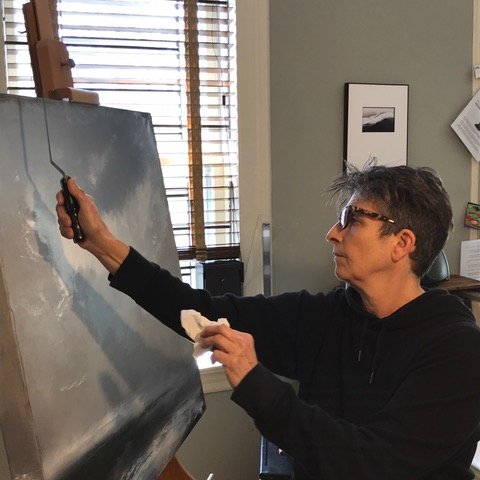 An artist works on her painting with a knife at the easel