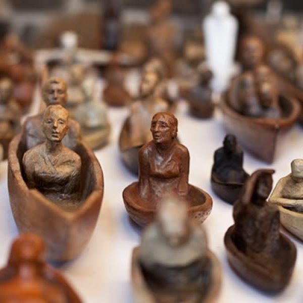 Small, terra-cotta boats carry people of various ages with different facial expressions.