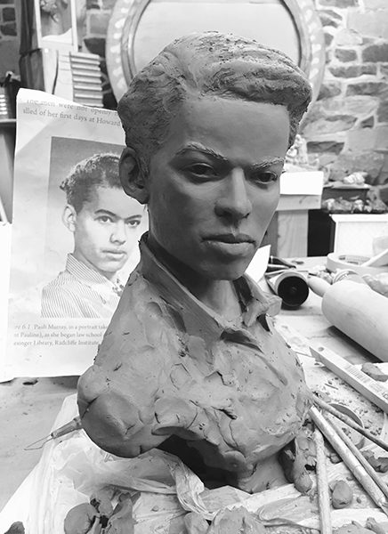 A black and white photo of a clay bust sculpture in process