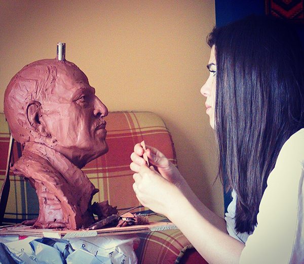 An artist works on a clay bust sculpture in progress