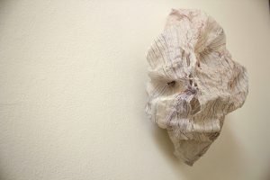 A paper and thread installation hangs on a gallery wall