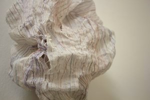 A paper and thread installation hangs on a gallery wall