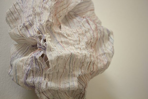 A close up of a paper and thread installation hung on a wall