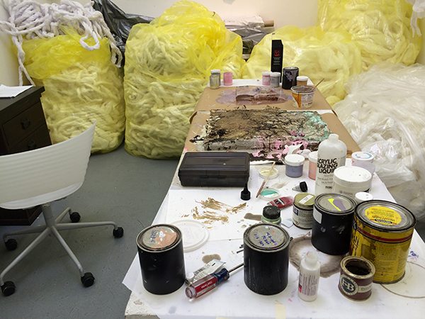 Weaving materials and paint scattered around an artist's studio