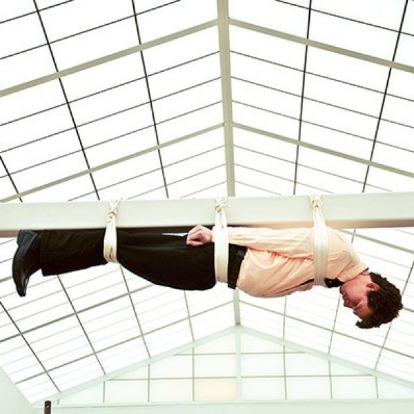 A performance art piece of a man hung from a beam across a high ceiling