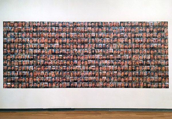 An installation of a collage of blurred images of a congressman or a congresswoman overlaid with the faces of fallen soldiers
