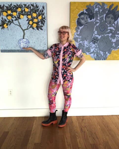 An artist stands in front of her colorful paintings