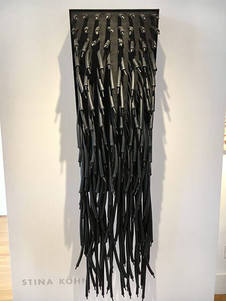 An installation on a wall of hanging black rubber tubing