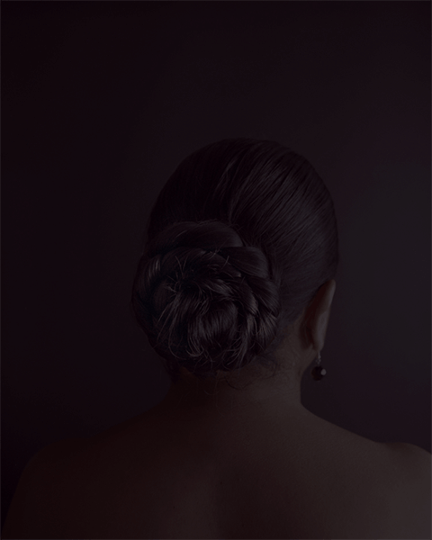 A portrait of a woman facing away from the viewer, so dark that the photo is almost black