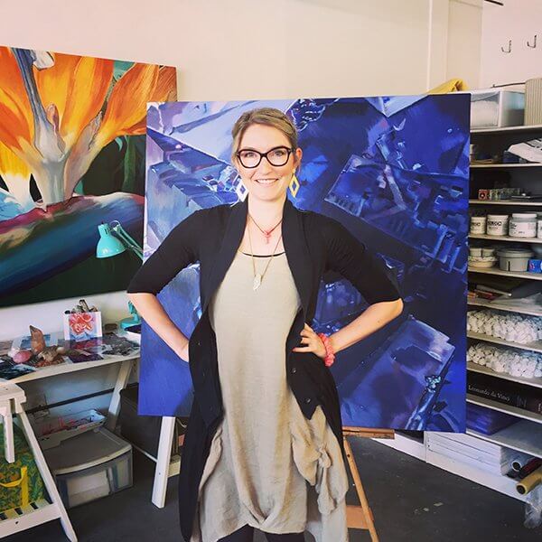 An artist poses in front of her large close-up paintings of flowers