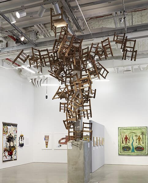 A sculptural installation including simple wooden chairs stacked on top of each other