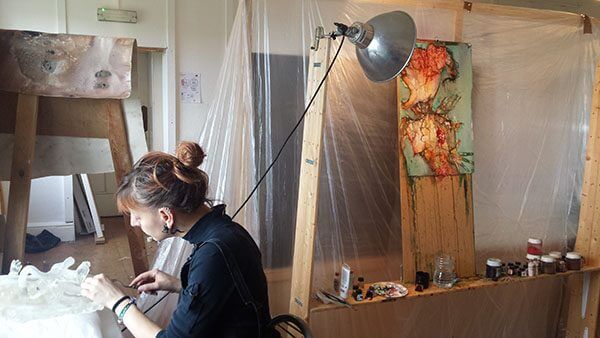 An artist sits at a table in her studio, working on her mixed media works