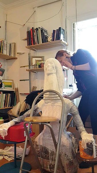 A mixed media artist works on a paper mache figure in her studio