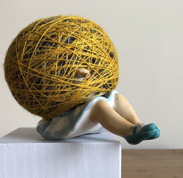 A sculpture of a female figure stuck inside a yellow bar of yarn