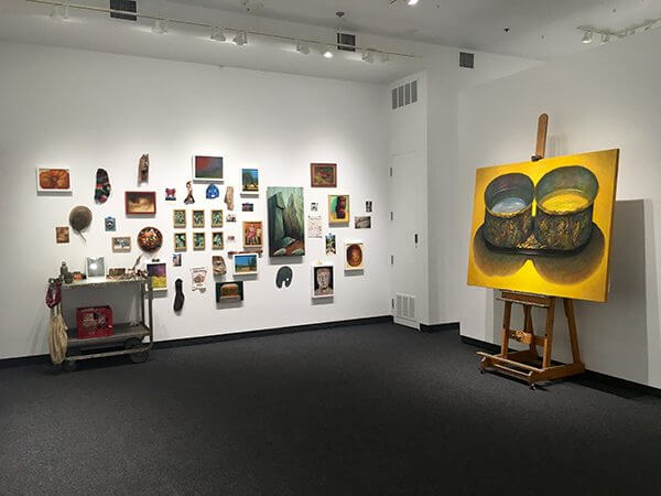 A painting on an easel and a collection of small hung paintings on a gallery wall