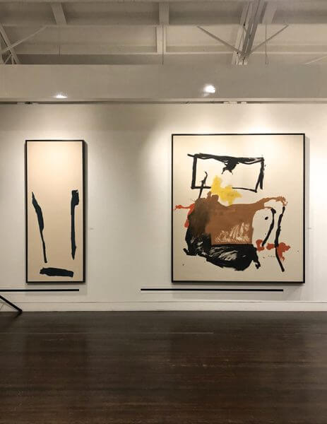 Two abstract paintings hanging on the walls of an art gallery