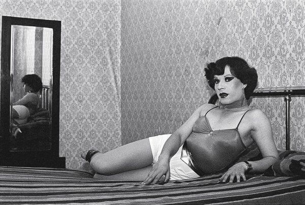 A black and white photograph of a man in drag laying on a bed